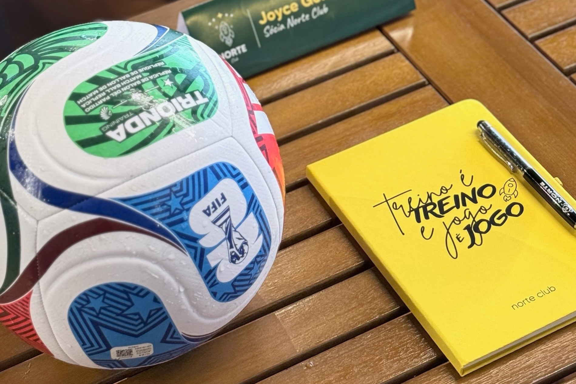 Bola oficial da FIFA ao lado do caderno amarelo 'Treino é treino e jogo é jogo' do Norte Club